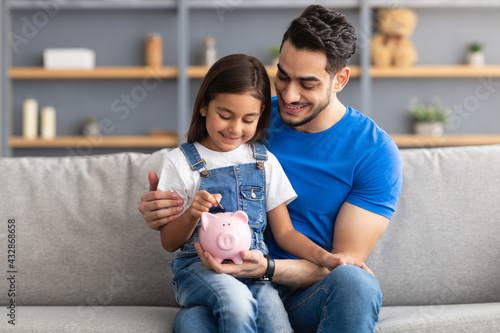 Fotografía Little girl and dad saving money in piggy bank