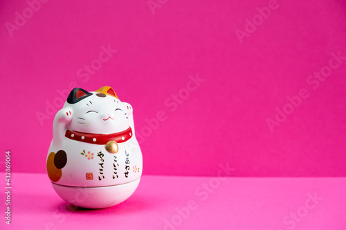 Maneki Neko ceramic asian japanese сat for good luck on pink background, symbolizing wealth