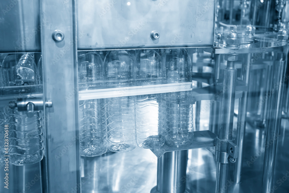 The PET bottles hanging on the conveyor belt for filling process in the drinking water factory. The hi-technology of plastic bottle manufacturing process. The PET bottles hanging on the conveyor belt for filling process in the drinking water factory. The hi-technology of plastic bottle manufacturing process.
