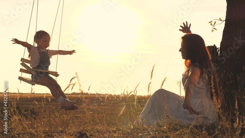 An adult woman rolls a child on a swing in the rays of the sunset in the sky, the concept of a happy family, the kid and the mother play outdoors in the plane, soar in the air and dream to fly
