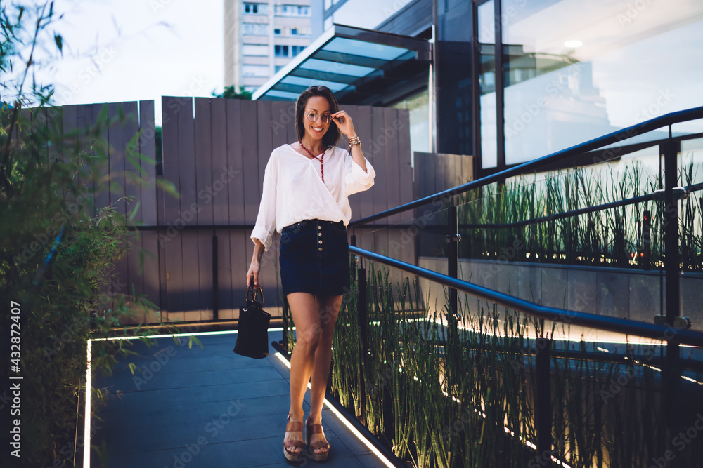 Obraz premium Carefree Caucasian female tourist in optical spectacles for provide eyes correction walking and smiling, happy woman 30 years old dressed in trendy clothing outfit enjoying leisure time in city