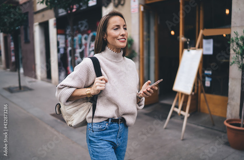 Pretty female tourist with travel backpack walking at urban street enjoying solo getaway vacations, happy Caucaisan woman with modern mobile technology in hand exploring new city during journey © BullRun