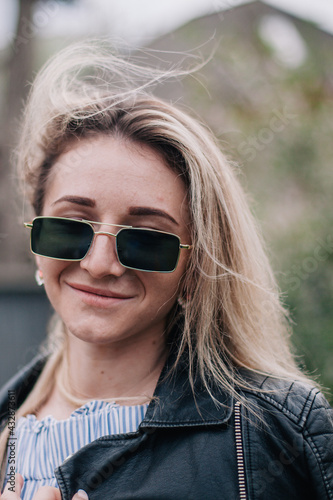 Young blonde in leather jacket and sunglasses posing in the street