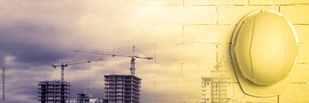 Yellow helmet on a brick wall against the background of buildings under construction. Workplace safety and health concept. Panoramic image, collage. Yellow helmet on a brick wall against the background of buildings under construction. Workplace safety and health concept. Panoramic image, collage.