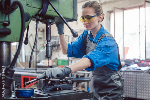 Woman worker in metal workshop greasing drill