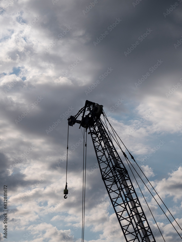 Silhouette of a large crane with hook with a blue and dark cloudy sky as a background Silhouette of a large crane with hook with a blue and dark cloudy sky as a background