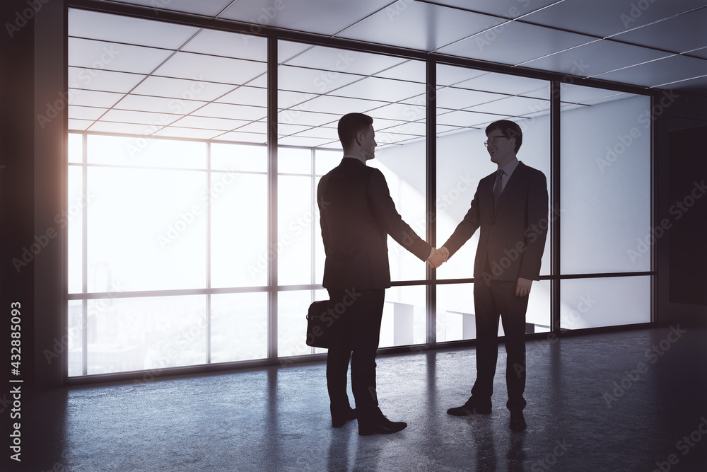 Business deal and partnership concept with businessmen handshaking in dark spacious office in sunny morning.