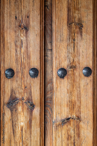 Antique wooden door with nails and knots. Rustic and retro old door full of knots and scratches. Vintage wood texture surface, wood vein. Pareidolia, faces in wood grain.