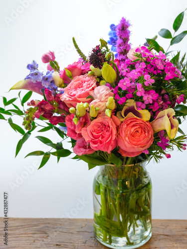Spring flowers bouquet in a glass vase. Pink roses, carnations, and wildflowers. Fresh uplifting flora on white background. © Naya Na