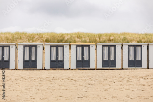 Graphic row of small closed square summer cubicle homes on Dutch North sea beach with dune behind on an overcast day  photo