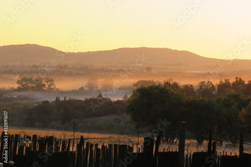 A picturesque sunset landscape photograph of two different colored mist cloud formations, white and orange, in front of hilltops under a orange streaky skyline in South Africa during autumn season