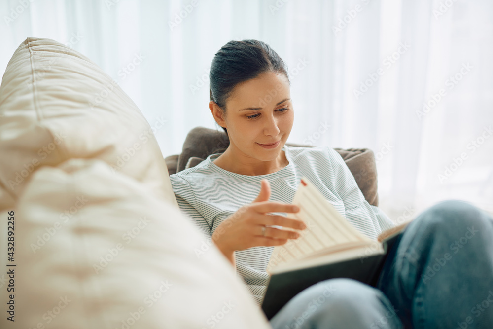 Smiling woman relaxing on the sofa and reading a book at home. Smiling woman relaxing on the sofa and reading a book at home.
