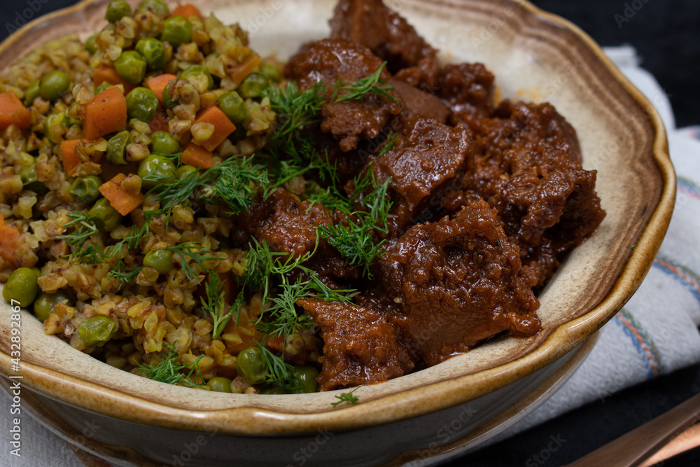 Vegan buckwheat and vegetables with seitan on plate, dark table, copy space Vegan buckwheat and vegetables with seitan on plate, dark table, copy space
