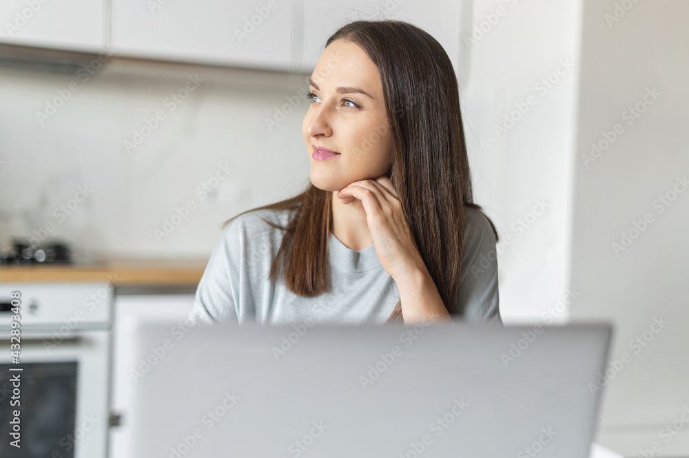 Remote work concept. Cheerful young woman using laptop computer for working from home, female freelancer taking a break and dreamly looks away sitting in the kitchen home, looks for inspiration Remote work concept. Cheerful young woman using laptop computer for working from home, female freelancer taking a break and dreamly looks away sitting in the kitchen home, looks for inspiration