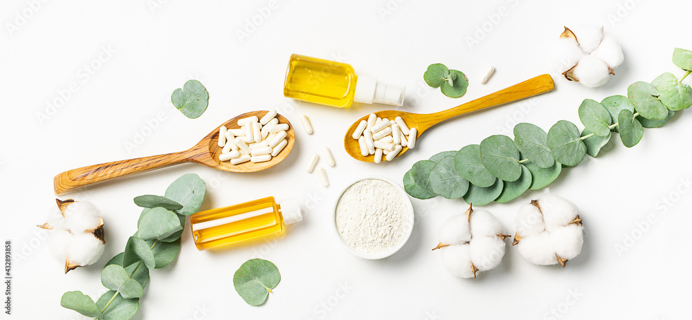 Eco organic cosmetic concept. Essential oils, collagen powder and capsules on white background with eucalyptus leaves and cotton flowers. Skin care concept.