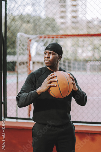 Black Spanish male in black casual clothes and do-rag holding a basketball ball on an outdoor court photo