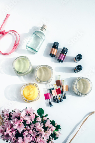 Cosmetic flasks, jars and bottles with essential oils, creams and fragrance layout with ribbons and flowers.