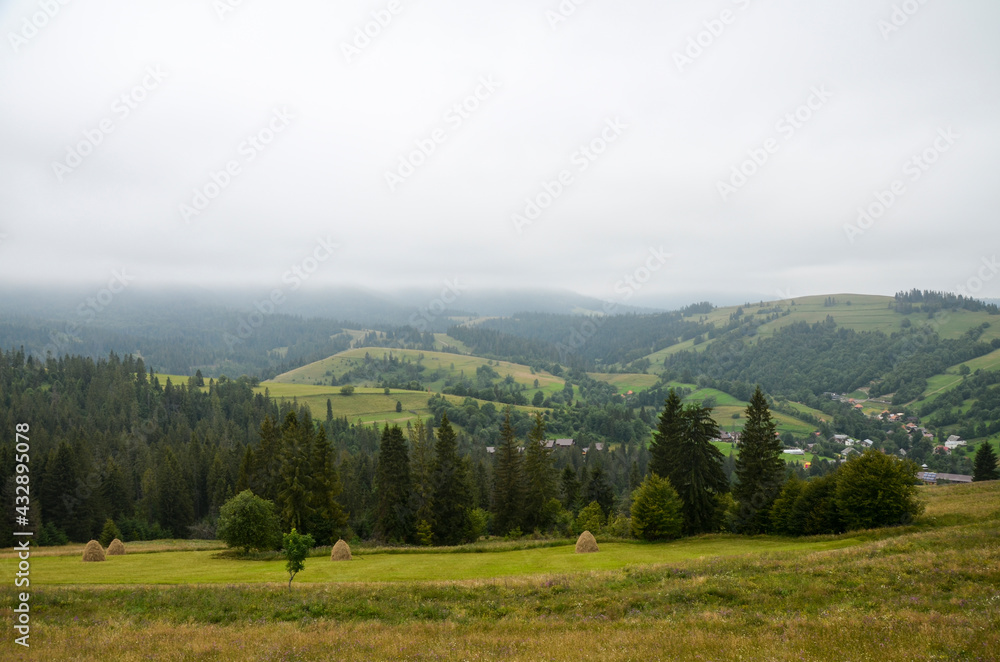 Beautiful view of village Izky with residential and under construction resort cottages in foggy valley, woody hills and mountains on horizon. Carpathians, Ukraine
