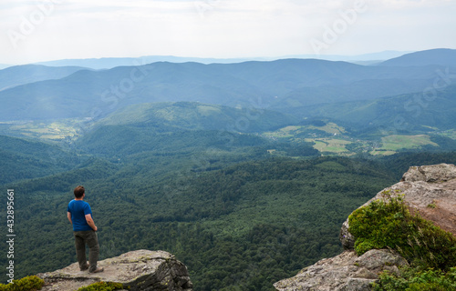 Man hiker stands over a cliff and enjoying a beautiful view of a green mountain valley. Freedom and travel concept. Carpathians, Ukraine