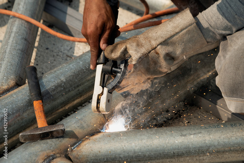 The welder is sitting on the steel roof frame and is welding..