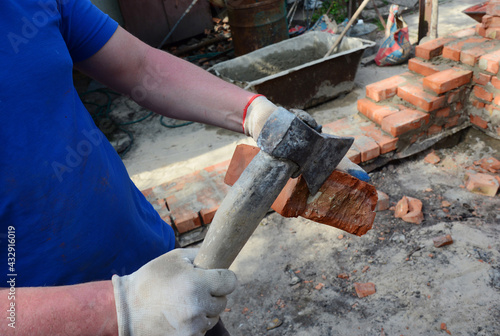 Masonry. How to hand cut a brick. A bricklayer is cutting a brick using a masonry tool, an axe while a brick wall, foundation construction.
