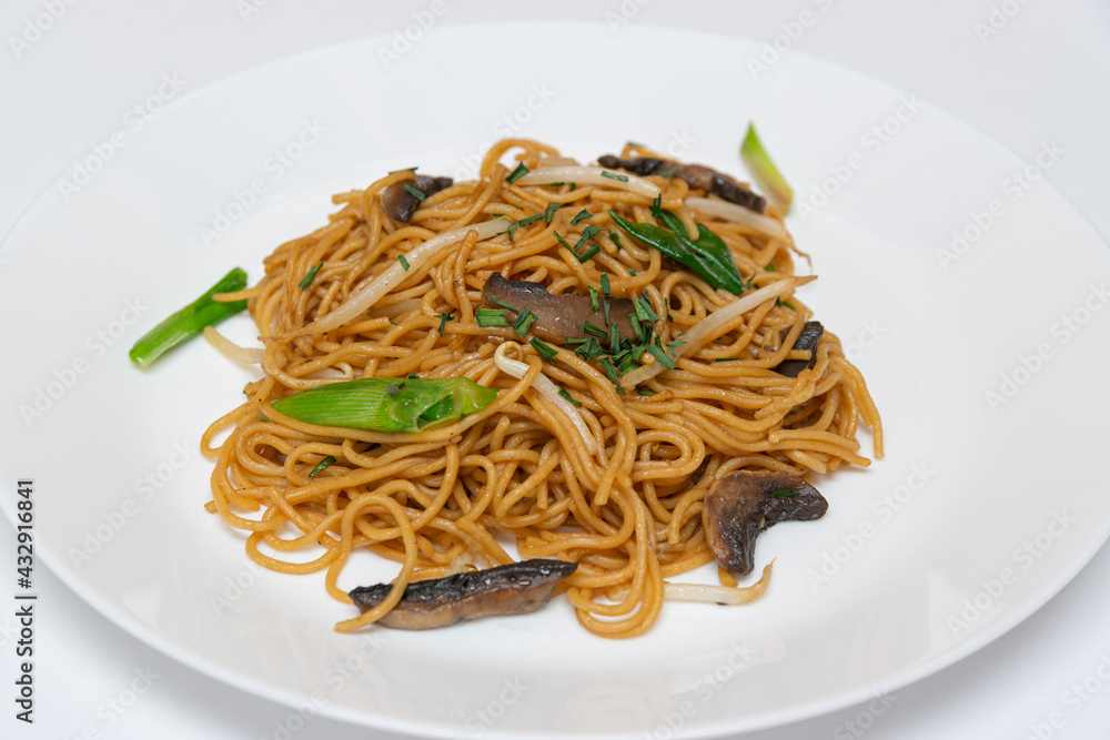 Fried noodles,Chow mein,with the addition of mushrooms and vegetables on a white plate.