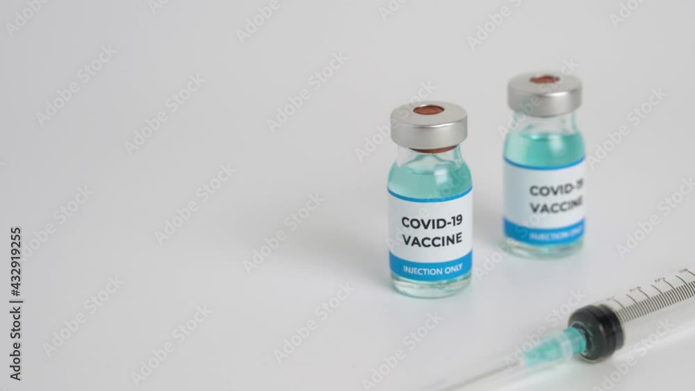 Close up of Covid-19 vaccine vials and syringe on white background. Hand takes one bottle of vaccine. Focus moves quickly to second bottle. Medical vaccination concept Close up of Covid-19 vaccine vials and syringe on white background. Hand takes one bottle of vaccine. Focus moves quickly to second bottle. Medical vaccination concept