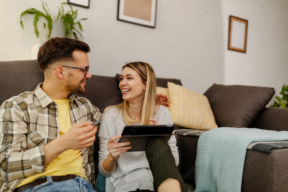 Obraz premium Cheerful couple making online order using tablet computer and credit card sitting on floor indoor.