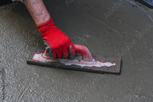 A man's hand in red gloves doing construction works on a cement ground home or outdoors on weekend or vacation