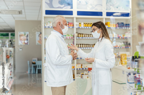 Side view of talking between two pharmacists and the corona virus. Before retiring, the pharmacist teaches the young pharmacist about working in a pharmacy. They wear uniforms and face masks