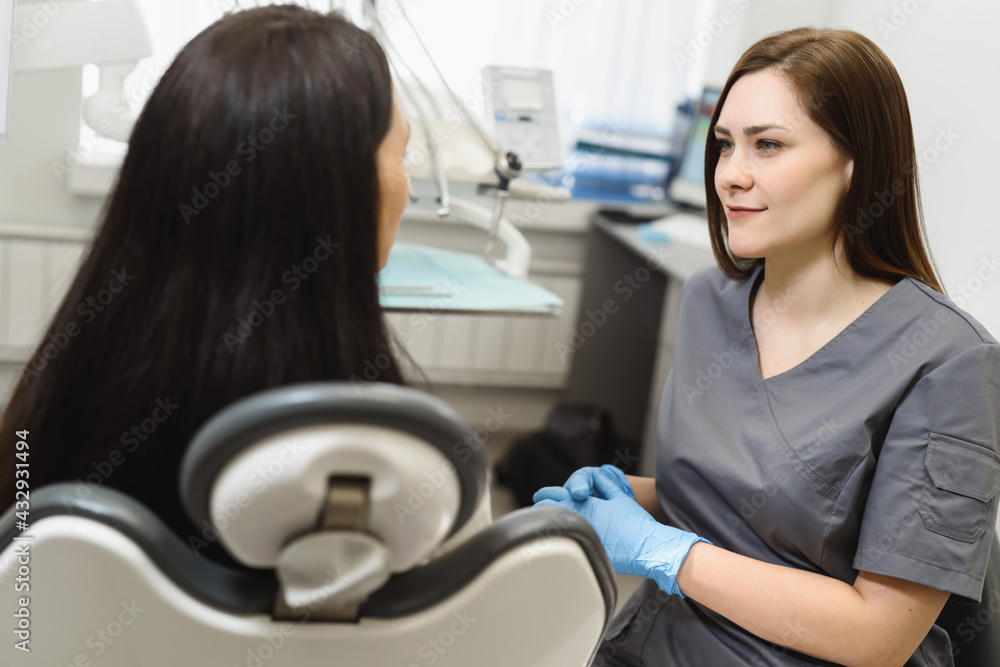 Friendly woman dentist consults a patient in an office in a modern dental clinic. The doctor listens attentively to the young woman Friendly woman dentist consults a patient in an office in a modern dental clinic. The doctor listens attentively to the young woman