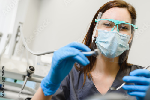 Female dentist at work in the clinic. A doctor wearing a face shield conducts a dental examination and treatment. First person shooting close-up