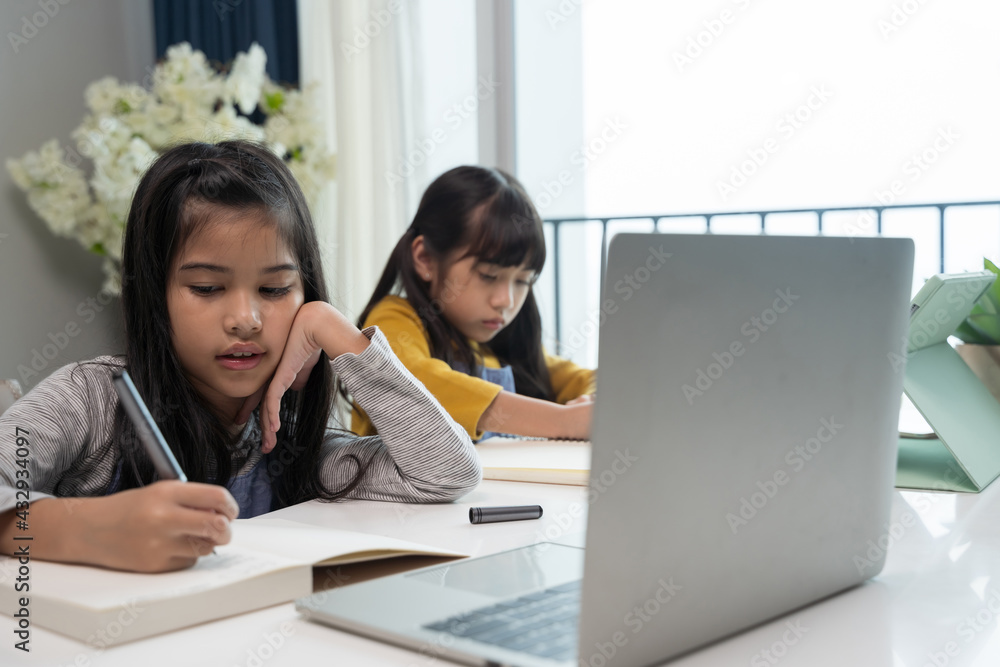 Little Asian girl studying online lesson at home with sister. Homeschooling during quarantine online education concept. Little Asian girl studying online lesson at home with sister. Homeschooling during quarantine online education concept.