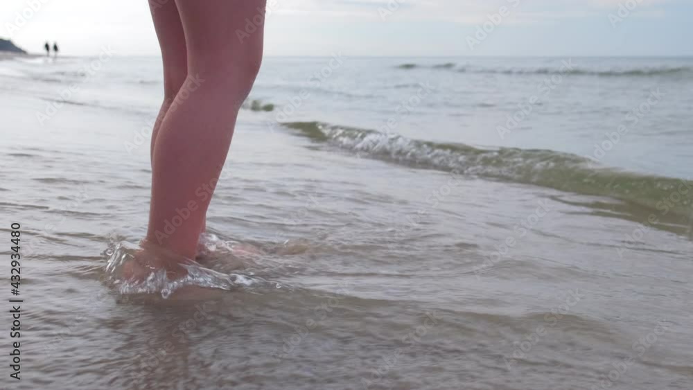 Young Caucasian Girl Standing on the Sea Shore with Waves Hitting Her Legs Young Caucasian Girl Standing on the Sea Shore with Waves Hitting Her Legs