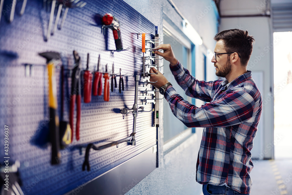 © Dusan Petkovic - Stacking tools in the workshop. A man dressed in a casual suit stands next to a tool board and tidies up the keys. Mechanical work indoor, repairing machine and cars