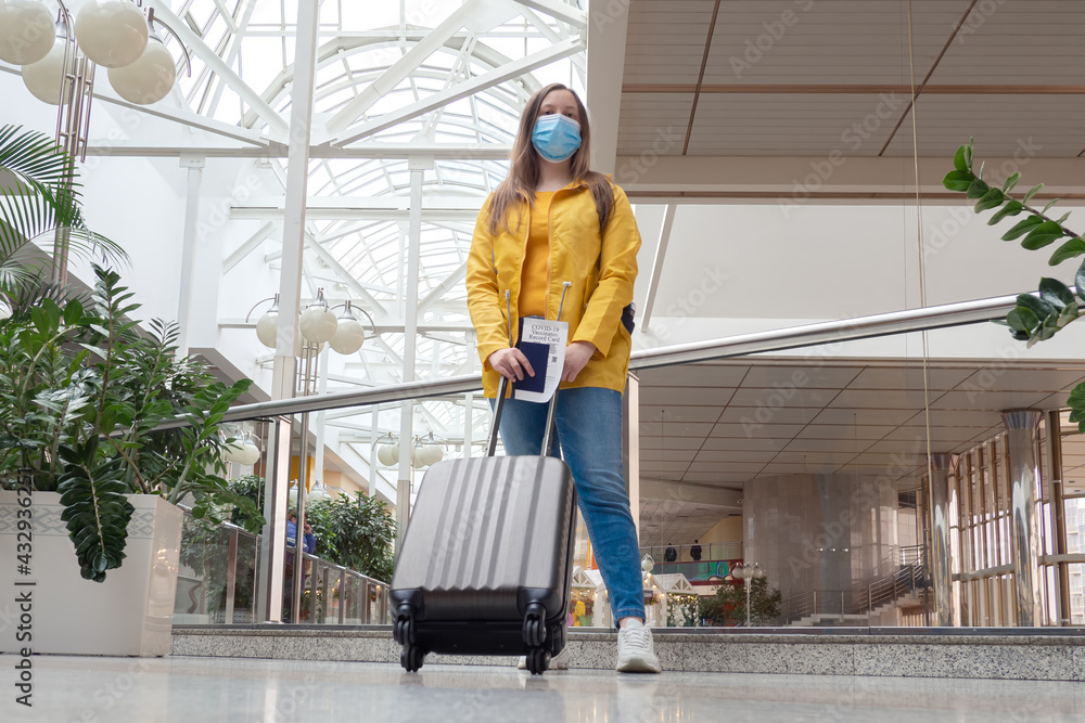 Fototapeta premium Traveler hold health passport and vaccination certification. woman with luggage stands at an airport train station. Safe travel concept, new normal for travelers.