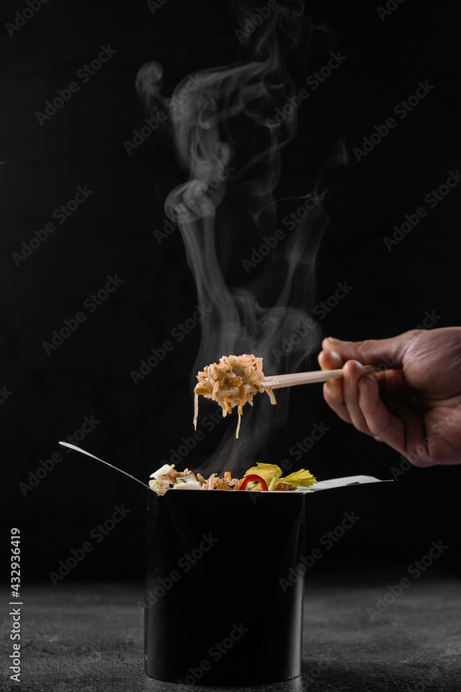 Steaming hot rice in wok box on black background. Holding rice with chinese chopsticks. Asian spicy dish for street restaurant and fast food delivery service. Steaming hot rice in wok box on black background. Holding rice with chinese chopsticks. Asian spicy dish for street restaurant and fast food delivery service.