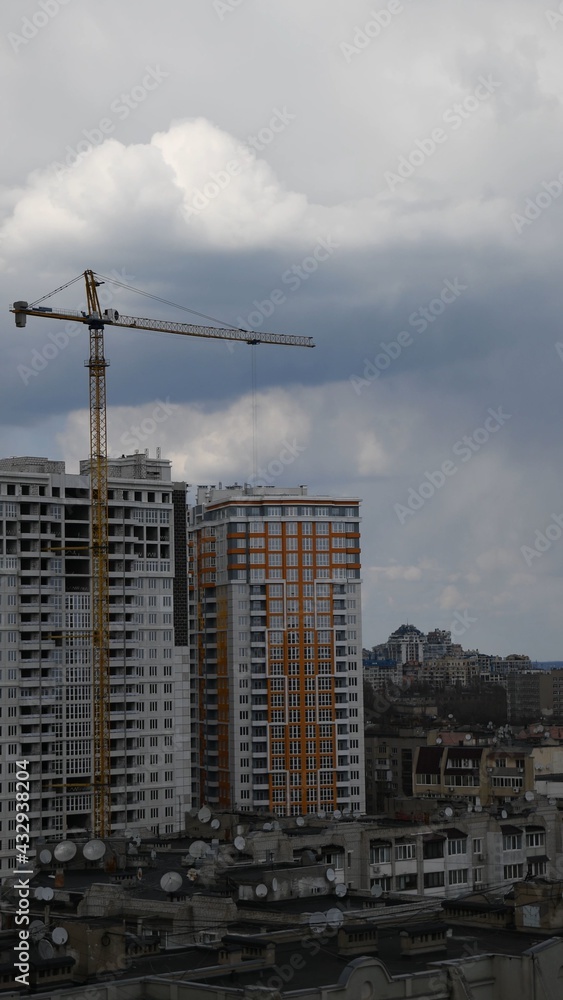 Construction site of unfinished multistory building with crane jib at overcast sky background. Under construction cityscape with rooftops and cloudscape. Vertical shot