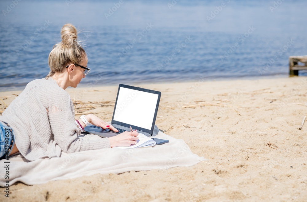 Woman working at a lake, using laptop. Freelance work, vacations, distance work, social distancing.