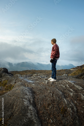 Hombre joven parado en la cima de una monta  a mirando el paisaje con la nubes azules de fondo