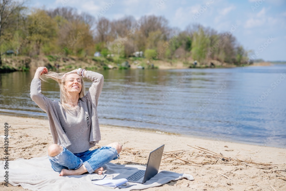 Happy free woman with laptop on the beach by the lake. Freelancer mobile office.