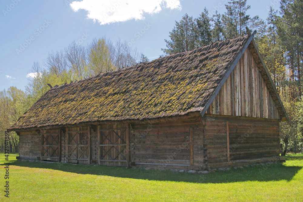 Old wooden barn, thatched. Overgrown with moss. He is standing on the green grass. Old rural construction. A village in Poland in Podlasie Old wooden barn, thatched. Overgrown with moss. He is standing on the green grass. Old rural construction. A village in Poland in Podlasie