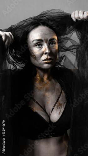 brunette with skin covered with paint in a photo studio on a gray background