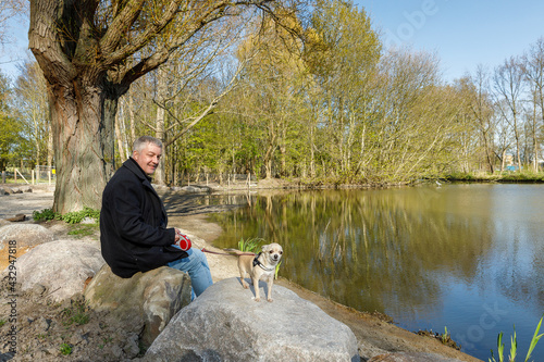 Man in black jacket with beige mini chihuahua dog puppy standing on rock near water, lake in Hoogvliet, dog beach in The Netherlands photo