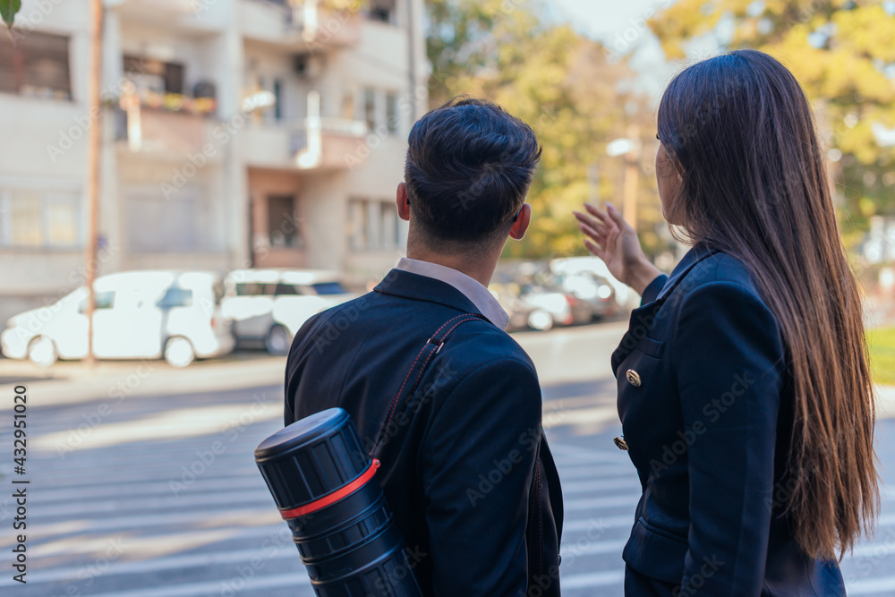Backview of suited male and female architects looking together at a building blueprint outside