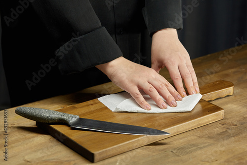 Cleaning of the workplace in the kitchen. Women's hands wipe the cutting board on the kitchen table