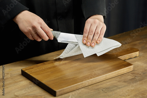 Cleaning of the workplace in the kitchen. Women's hands wipe a kitchen knife