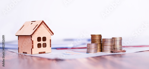 wooden house and pyramids of coins stand on a wooden table