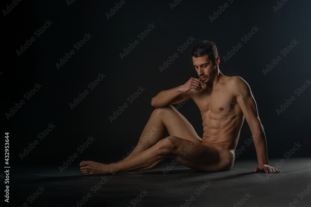 Fashion nude photo of a male model with seductive figure sitting isolated on the floor in a studio Fashion nude photo of a male model with seductive figure sitting isolated on the floor in a studio