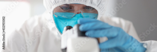 фотографія Doctor in protective suit and glasses looks through microscope